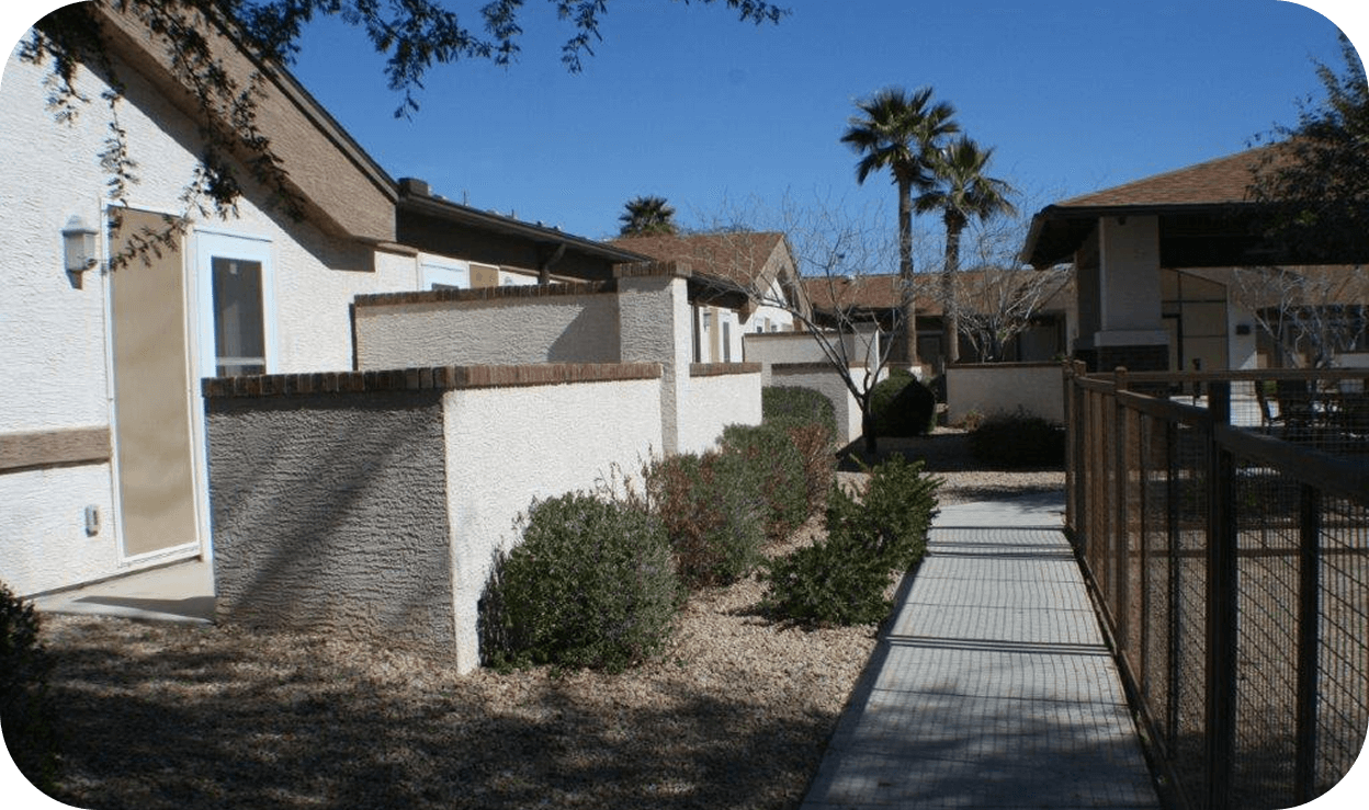 Exterior of a complex of single level apartment homes with palm trees surrounding the center