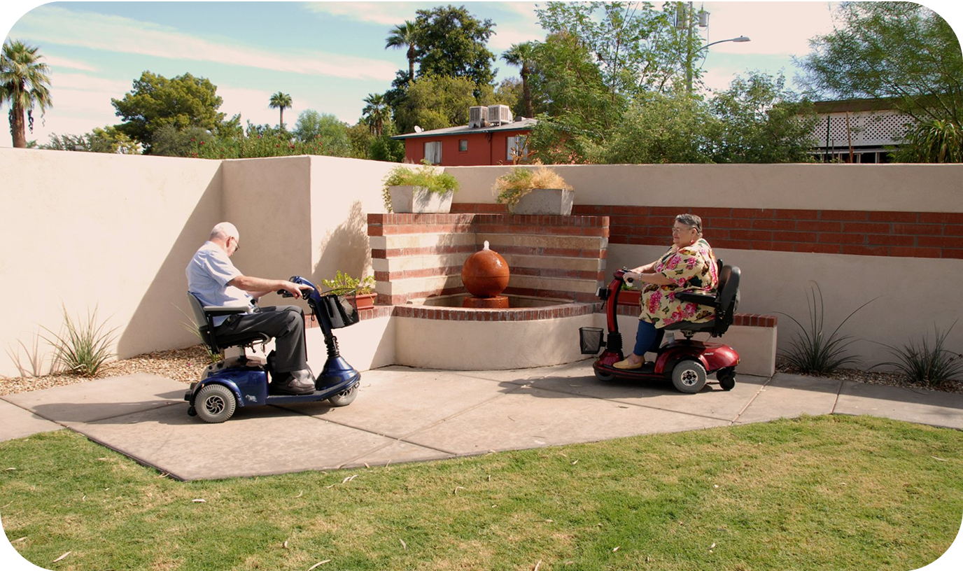 Image of two elderly people riding their mobile scooter in the backyard