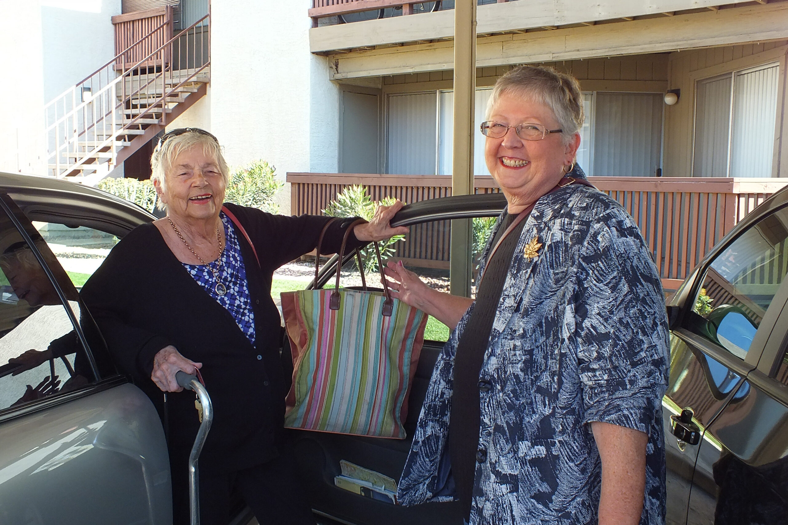Two older women smiling at the camera standing next to one another