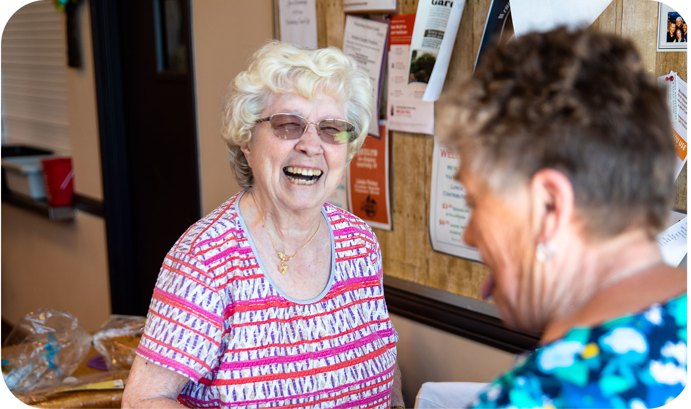An elderly woman smiling at the camera while standing next to a bulletin board in an office