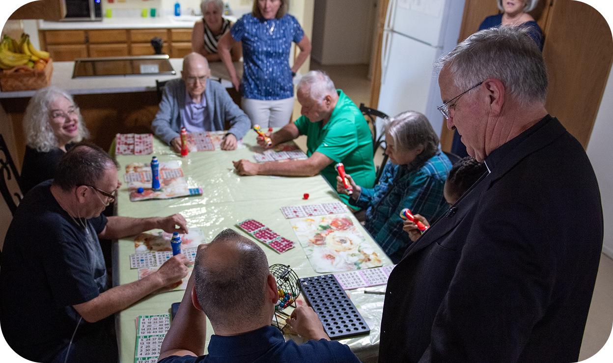 A group of 9 elderly people gathered around a table playing bingo